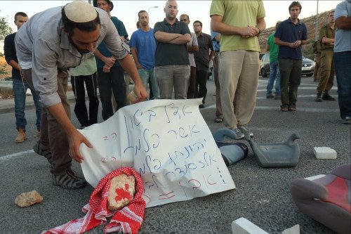 Photo: Hillel Maeir, Tazpit News Agency / An Israeli man holds a sign with names: Adele Biton, Asher Palmer, Jonathan Palmer, and Alexander Levlovitz, all victims of Palestinian rock attacks on the road. 